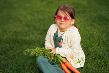 little girl farmer with vegetables and pumpkin on the background of green grass and vegetable garden. healthy eating concept.