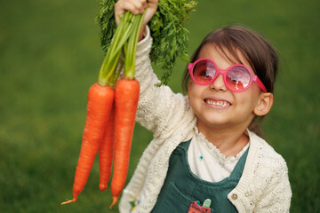 little girl farmer with vegetables and pumpkin on the background of green grass and vegetable garden. healthy eating concept.