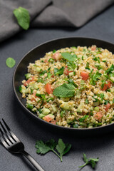 Bulgur tabbouleh salad with parsley, mint, cucumber, tomato in a black bowl on a dark background with copy space