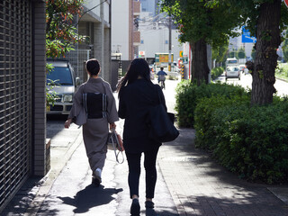 秋の朝の都市の道路で歩く着物女性とスーツ姿女性の様子