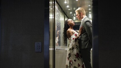 A handsome young man and a beautiful woman look at each other and smile while standing in an elevator. A couple of lovers tenderly touch each other in an elevator