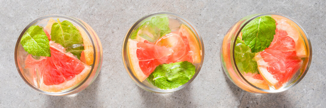Refreshing grapefruit drink with mint leaves and ice on gray stone table