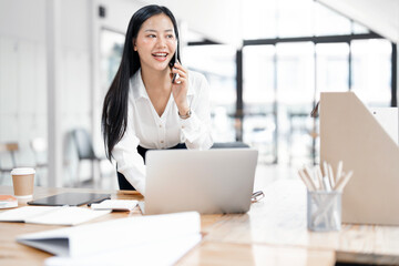 Happy asian businesswoman talking on mobile phone while working with her project in office.