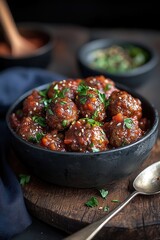 A rustic bowl filled with savory meatballs coated in a rich sauce showcases the dishs vibrant colors. Freshly chopped herbs add a pop of green, while accompanying dipping sauces sit in small bowls nea