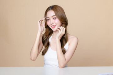 Young Asian beauty woman curly long hair with korean makeup style touch her face and perfect skin on isolated beige background. Facial treatment, Cosmetology, plastic surgery.