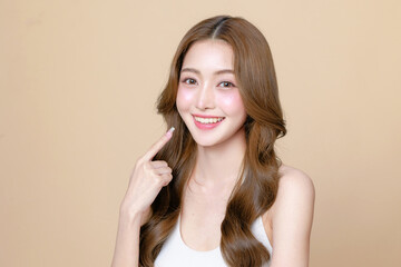 Young Asian beauty woman curly long hair with korean makeup style touch her face and perfect skin on isolated beige background. Facial treatment, Cosmetology, plastic surgery.