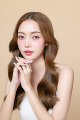 Young Asian beauty woman curly long hair with korean makeup style touch her face and perfect skin on isolated beige background. Facial treatment, Cosmetology, plastic surgery.