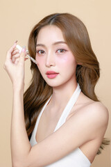 Young Asian beauty woman curly long hair with korean makeup style on face and using pipette to apply serum on skin on isolated beige background. Facial treatment, Cosmetology, plastic surgery.