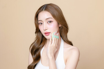 Fototapeta premium Young Asian beauty woman curly long hair with korean makeup style touch her face and perfect skin using puff on isolated beige background. Facial treatment, Cosmetology, plastic surgery.