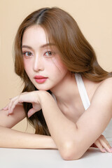Fototapeta premium Young Asian beauty woman curly long hair with korean makeup style touch her face and perfect skin on isolated beige background. Facial treatment, Cosmetology, plastic surgery.