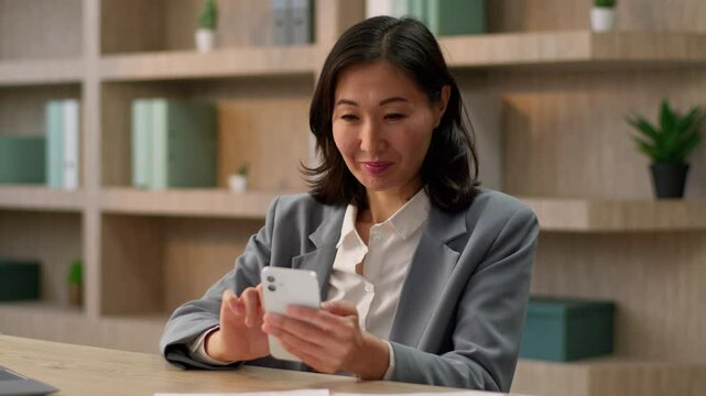 Thoughtful Asian woman businesswoman employer business girl female worker chinese japanese korean lady work in office using mobile phone gadget addict thin message typing browsing smartphone internet