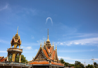 Fototapeta premium Traditional Thai temple architecture with intricate gold details under a bright blue sky, featuring a unique arch-shaped cloud above the temple, capturing cultural heritage and a serene, atmosphere.