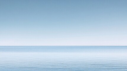 Fototapeta premium A tranquil scene of a calm sea with a clear blue sky above. The water is a light blue and the sky is a soft white. The horizon is a thin line where the two meet.