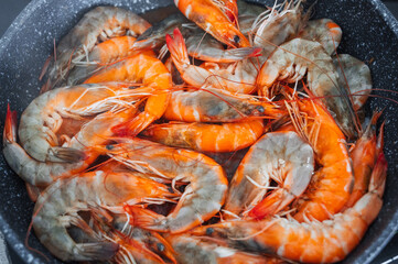 A close-up view of the undivided shrimp fried in oil in a frying pan.