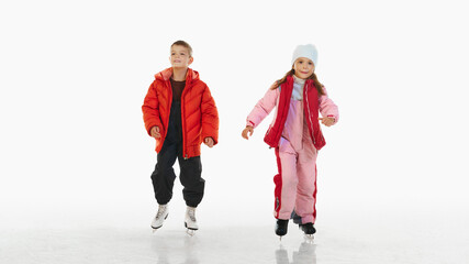 Happy young boy and girl, brother and season wearing red winter jackets, enjoying ice skating, isolated on white background. Concept of winter, vacation, holiday, leisure activity