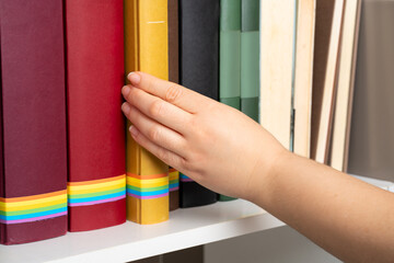 Happy young woman removing a book with rainbow flag from a shelf in a college library
