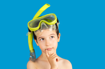 Pensive boy with snorkel mask tuba and snorkel looks away at copy space thinking isolated on a blue...