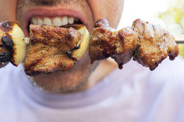 A man eats a juicy fragrant piece of pork kebab on a skewer. Fatty calorie foods