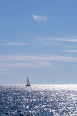A sailboat with white sails glides across a vast expanse of sparkling blue water. 