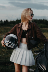 Obraz premium portrait of a girl next to a motorcycle. She holds a helmet in her hands. blurred focus