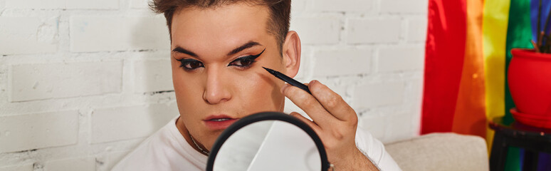 A queer person applies eyeliner with focus, surrounded by colorful decor that celebrates diversity.