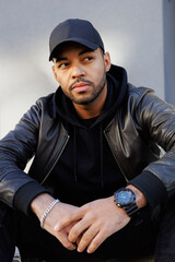 Portrait of stylish african american man in baseball cap and leather jacket outdoors