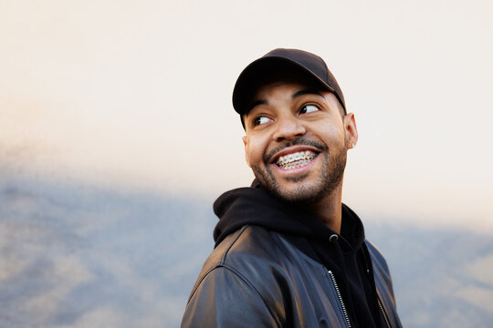 Portrait of cheerful african american man in baseball cap  standing near wall with shadow 