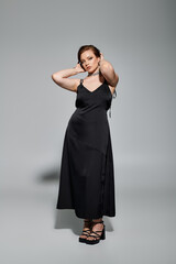 Fototapeta premium A young woman poses elegantly in a stunning black dress, exuding confidence and style.