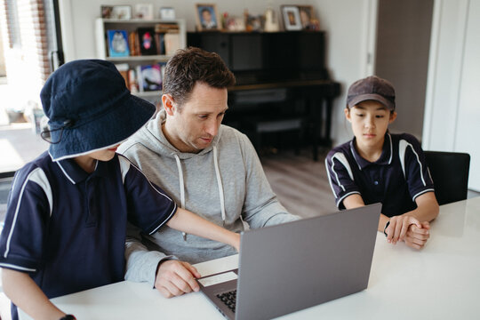 Dad helping kids with their homework using laptop.