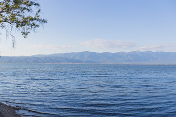 Tranquil Scene Of Doirani Lake With Its Calm Waters Stretching To The Horizon, Framed By Distant Mountain Ranges And A Clear, Blue Sky