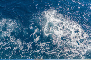 Sunlight glistens on deep blue ocean waves, with seafoam adding a dynamic texture and sparkle.