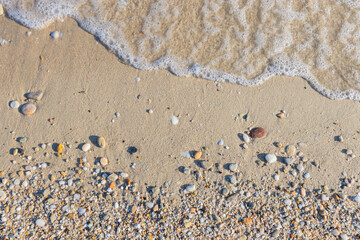 A close-up of pebbles and seafoam at the sandy shoreline, creating a peaceful beach scene.