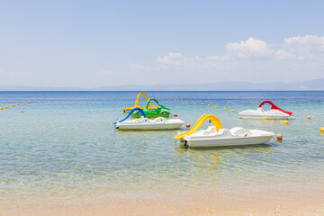 Serene beach scene featuring colorful pedal boats floating on calm, crystal-clear waters.