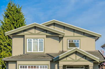 Top of grey stucco luxury house with shingle roof, red and yellow trees and nice windows in Summer in Vancouver, Canada, North America. Day time on June 2024.