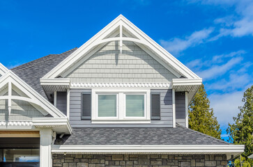 Top of grey stucco luxury house with shingle roof, red and yellow trees and nice windows in Summer in Vancouver, Canada, North America. Day time on June 2024.