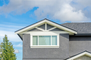 Top of grey stucco luxury house with shingle roof, red and yellow trees and nice windows in Summer in Vancouver, Canada, North America. Day time on June 2024.