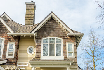 Top of grey stucco luxury house with shingle roof, red and yellow trees and nice windows in Summer in Vancouver, Canada, North America. Day time on June 2024.