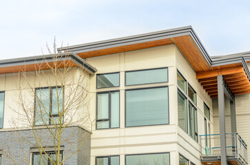 Top of grey stucco luxury house with shingle roof, red and yellow trees and nice windows in Summer in Vancouver, Canada, North America. Day time on June 2024.