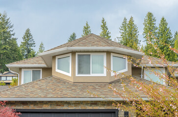 Top of grey stucco luxury house with shingle roof, red and yellow trees and nice windows in Summer in Vancouver, Canada, North America. Day time on June 2024.