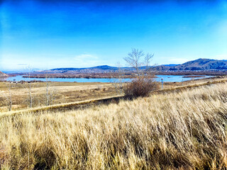 Serene landscape with a calm river and distant hills under a clear blue sky during a sunny day in early spring