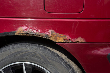 Rusty car. Red old rusty car. Fragment of a red wing of an old car. Rusty hole in metal