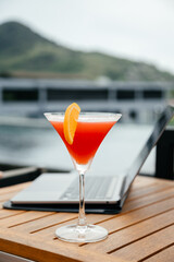 Laptop and glass of refreshing red cocktail on a table background. Work and travel or remote business concept.. Out of office work concept. Free copy space, vertical shot