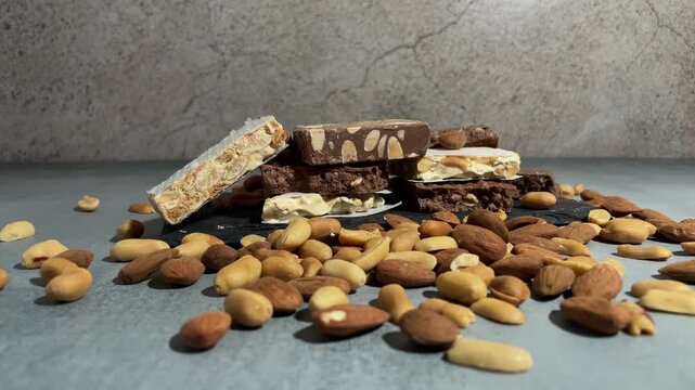 A close-up view of assorted nougat bars, featuring layers of chocolate, almonds, and peanuts arranged on a slate, showcasing texture and variety