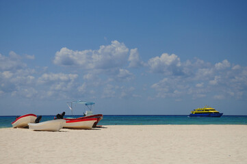 Fototapeta premium Beach scene: boats on shore, ferry in turquoise ocean under cloudy sky