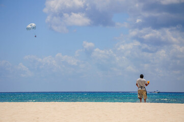 Person at serene beach with parasailing in the background under blue sky