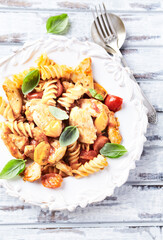 Pasta with chicken breast, cherry tomatoes and fresh basil. Bright wooden background. Close up.	