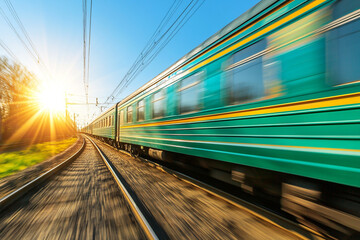Fototapeta premium A green and blue train is moving rapidly on the railway, with a motion blur effect.