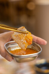 A woman's hand picks up grilled pork with chopsticks and dips it in a delicious sauce.