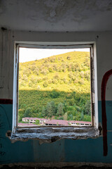 Framed view of green hills through an abandoned window in a decaying building