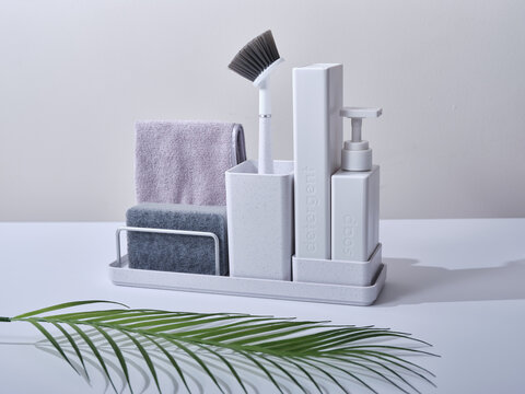 White sink organiser on a white background with a palm leaf on the counter